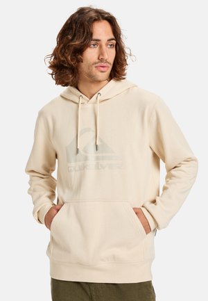 Sudadera con capucha beige que cuenta con un bolsillo frontal, cordones ajustables y un logotipo sutil impreso en el pecho. Textura de tela suave.