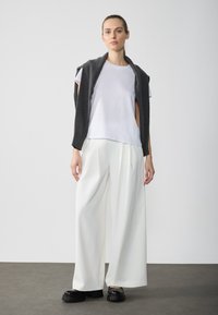 White t-shirt layered under a dark gray sleeveless knit top, paired with loose white trousers and chunky black platform shoes.