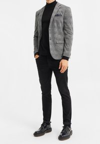 Grå rutiga kavaj över en svart polotröja, tillsammans med svarta jeans och svarta skor. Anmärkningsvärd fickhandduk med vita prickar.