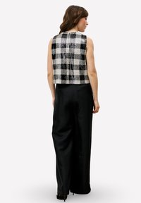 Kort gesneden, mouwloos topje met een zwart-wit geruit patroon; de stof heeft een getextureerde afwerking; gecombineerd met losse zwarte broek.