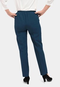 Donkergroene, taps toelopende broek met een elastische tailleband, zijnaden en een soepele textuur, gecombineerd met zwarte hoge hakken.