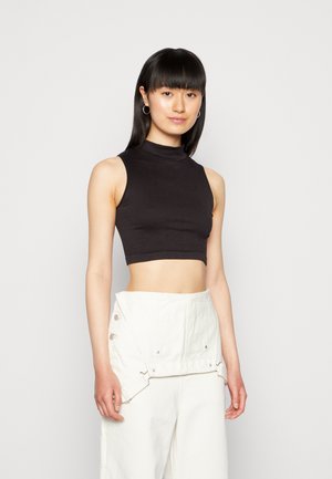 Top cropped preto canelado com gola alta, combinado com calças largas de tom claro com botões laterais e um design dobrado.