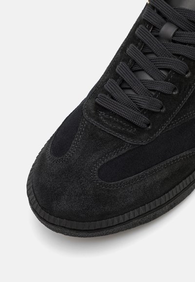 Black suede sneaker with textured surface, smooth accents, black laces, and a rubber sole featuring a ribbed edge.