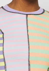 Ribbed short-sleeve top featuring stripes in pastel colors: pink, green, lavender, and orange, with contrasting black stitching and a rounded neckline.