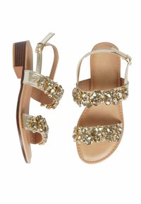 Sandali oro e beige con due cinturini gioiello, caratterizzati da decorazioni trasparenti e in oro chiaro e un tacco basso in legno. Finitura in pelle liscia.