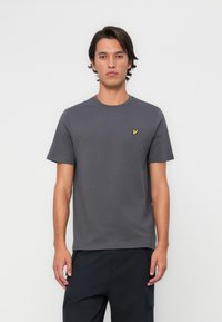 Szary t-shirt z okrągłym dekoltem, wykonany z bawełny, z krótkimi rękawami i małym, żółtym haftowanym logo po lewej stronie klatki piersiowej.
