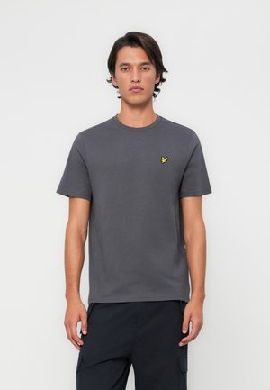 T-shirt gris à col rond en coton, avec des manches courtes et un petit logo brodé jaune sur la poitrine gauche.