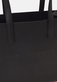 Czarna torba na ramię, materiał teksturowany, wytłoczone logo "TED BAKER LONDON", podwójne uchwyty, strukturalny kształt, minimalistyczny design, brak dodatkowych akcentów.