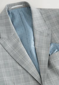 Grau kariertes Sakko mit Revers, hellblauer Futterung mit kleinen schwarzen Punkten und einer Brusttasche mit passendem Taschentuch.