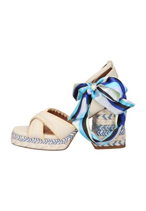 Sandali platform beige con suole intrecciate blu e bianche, cinturini larghi e un fiocco a righe blu, nero e bianco legato alla caviglia.