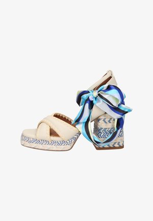 Sandali platform beige con suole intrecciate blu e bianche, cinturini larghi e un fiocco a righe blu, nero e bianco legato alla caviglia.