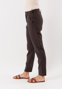 Pantaloni marroni, su misura, con una vestibilità rilassata, dotati di vita piatta e tasche laterali. Abbinati a sandali marroni.