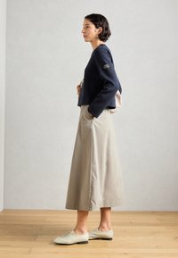Suéter corto azul marino de mangas largas, falda beige hasta la rodilla y zapatos gris claro. Presenta un parche en el suéter y bolsillos en la falda.