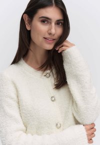 Witte textuur cardigan met een ronde halslijn, voorzien van twee zilveren en parel knopen, lange mouwen en een zachte, fluffige uitstraling.