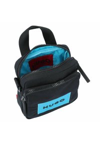 Borsa di stoffa nera con una toppa logo blu, chiusura a zip e manico superiore. L'interno presenta una fodera blu brillante e un'etichetta rossa.