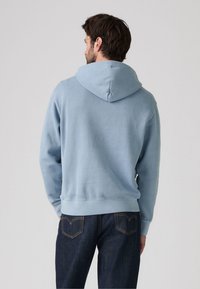 Lys blå hettegenser med snorhette, myk tekstur og ribbet kant. Brukt med mørk denim jeans, viser en enkel bakdesign.