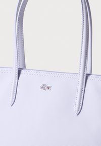 Ljuslila tote bag i texturerat material, med två släta handtag och en liten broderad logotyp av en krokodil.