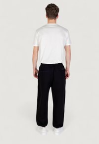 Witte T-shirt met korte mouwen, gecombineerd met zwarte sportbroeken met achterzakken en een elastische tailleband, gedragen met witte sneakers.