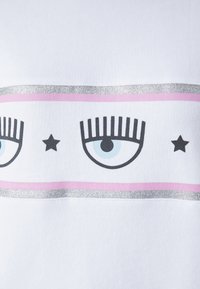 Vit sweatshirt med en design som har två stiliserade ögon, svarta fransar, ljusblå irisar och en silverkantad rosa rand med stjärnor.