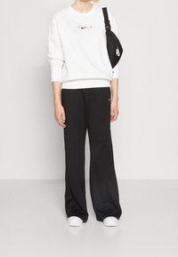 White sweatshirt with orange Nike logo, paired with black wide-leg pants featuring a small Nike logo. White shoes complete the outfit.