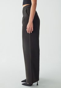 Vysoké černé kalhoty s rovnými nohavicemi, vyrobené z texturované látky. Mají elegantní povrchovou úpravu a jemné detaily v bočních švech.