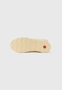 Beige rubber shoe sole with a wavy tread pattern and a prominent red circular accent. Features branded texture and a smooth surface.