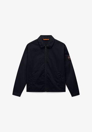 Veste noire zippée avec col, manches longues, poches latérales, et un patch logo circulaire sur la partie supérieure de la manche gauche.