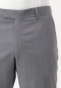 Pantalons gris texturés avec un motif à carreaux subtil, présentant une coupe droite et une taille standard. Le matériau a un léger éclat.