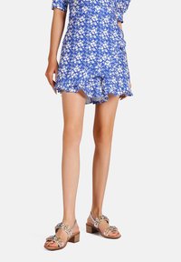 Abito blu floreale con orlo a scalloping abbinato a sandali metallici con gioielli decorativi e tacco a blocco.