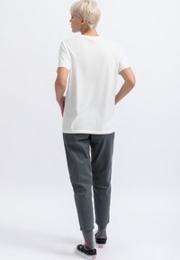 Witte katoenen t-shirt met een ronde hals, gecombineerd met grijze tapered broeken en zwarte sneakers, met een subtiele logoprint op de rug.