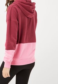 Hooded sweatshirt with a maroon top section and a pink lower section. Made of soft fabric with ribbed cuffs and hem.