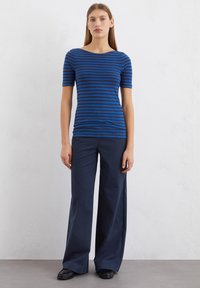 Gestreiftes Kurzarm-Oberteil in Blau und Marineblau mit einem Bootsausschnitt, kombiniert mit dunklen, weit geschnittenen Hosen und schwarzen flachen Schuhen.