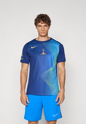 T-shirt de sport bleu avec des lignes dynamiques bleu clair et vert, arborant un logo de club sur la poitrine et un emblème Nike en forme de virgule. Accompagné d'un short bleu vif.