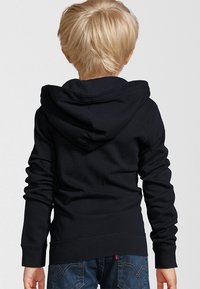 Zwarte hoodie met een kangoeroezak, ribbelmanchetten en onderrand. Zachte stof; de achterkant toont de capuchon en een glad, effen textuur.