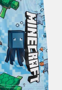 Blå badshorts med pixelerade Minecraft-motiv, inklusive en bläckfisk, sköldpaddor och ordet "Minecraft" i fet svart text.