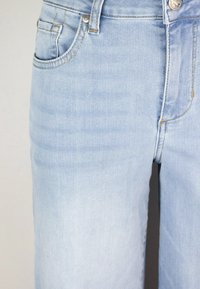 Jeans in denim azzurro chiaro con una finitura leggermente sbiadita. Dotati di una tasca anteriore e chiusura con bottone metallico, evidenziando i dettagli delle cuciture.