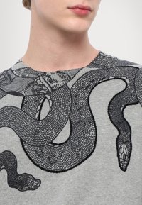 T-shirt in cotone grigio con un'illustrazione dettagliata di un serpente nero. Collo tondo, maniche corte e una texture liscia.