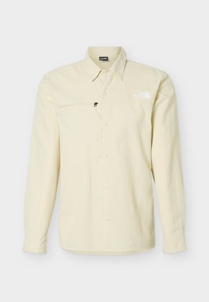 Hellbeige Langarmbluse mit Knopfleiste vorne, Reißverschlusstasche auf der Brust und The North Face Logo auf der linken Brustseite.