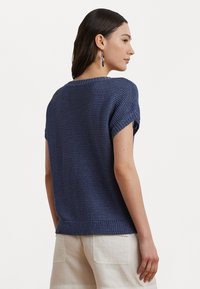Suéter de punto azul marino de manga corta, con un patrón texturizado, cuello redondo y dobladillo acanalado. Combinado con pantalones holgados de color claro.