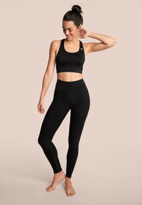 Schwarzer Sport-BH und hochgeschnittene Leggings aus dehnbarem Material. Das Outfit zeichnet sich durch ein einfaches Design ohne sichtbare Muster oder Hardware aus.