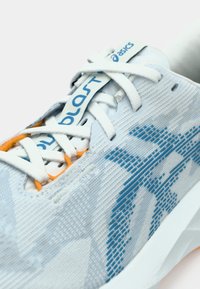 Light blue running shoe with a textured upper, featuring a blue patterned design, white laces, and an orange accent near the eyelets.