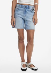 Shorts de mezclilla azul claro con un corte relajado, presentan bordados florales en los bolsillos delanteros y un diseño clásico de cinco bolsillos.
