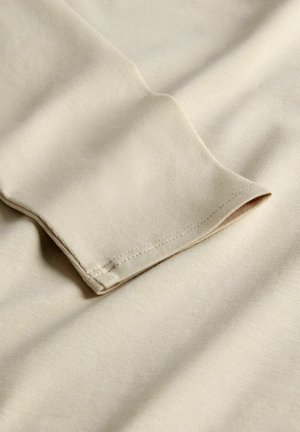 Beige bavlněná tkanina s hladkým povrchem, zdobená ohnutým manžetovým rukávem a jemným šitím. Měkká, lehká a odolná proti mačkání.