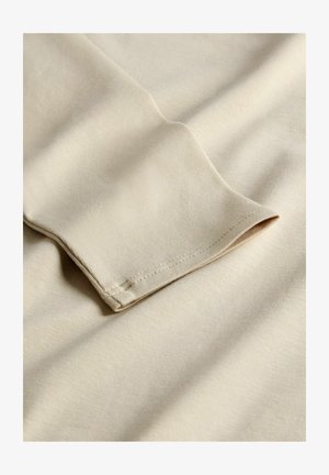 Beige cotton fabric with a smooth texture, featuring a folded cuff and subtle stitching details. Soft, lightweight, and wrinkle-resistant.