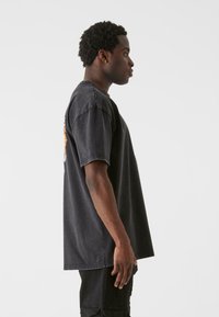 Sort oversized t-shirt lavet af bomuld, med rund halsudskæring og korte ærmer. Stoffet har en let slidt tekstur.