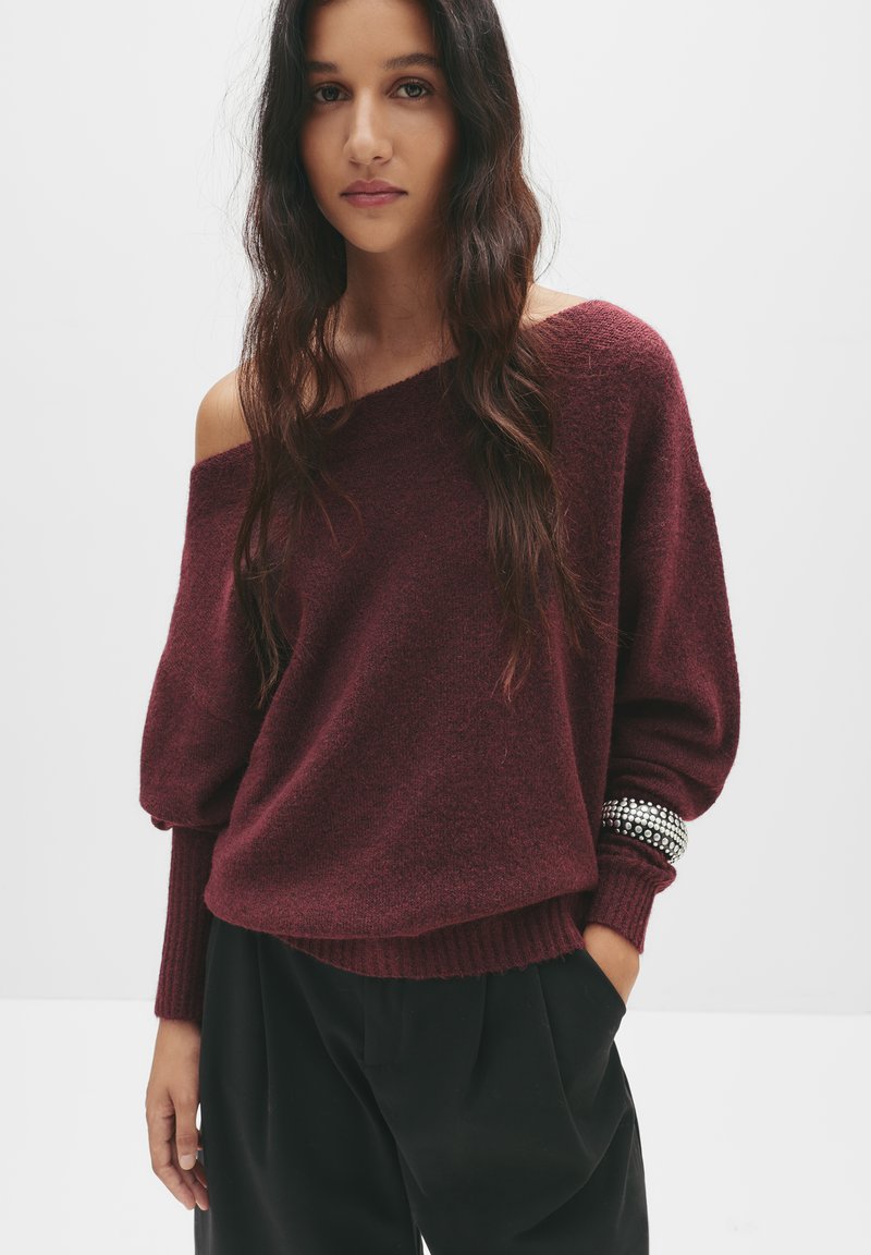 Bordeaux, oversized gebreid sweater met off-shoulder ontwerp en geribde manchetten. Beschikt over een gestructureerde afwerking en versierde armbanden.