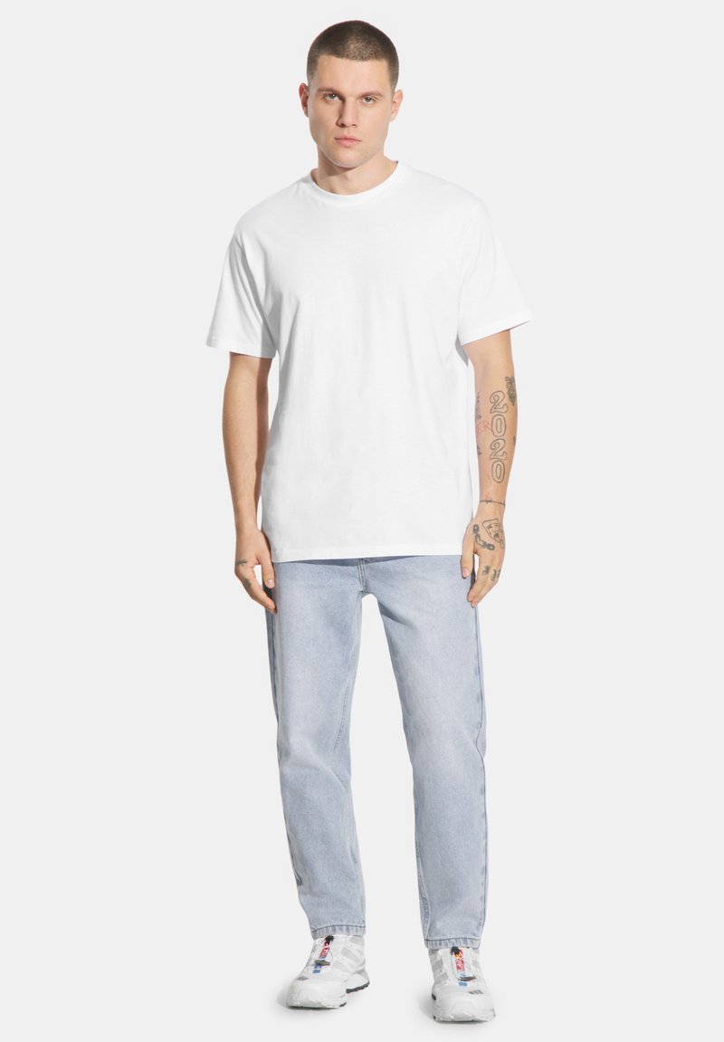 Biała bawełniana koszulka z krótkim rękawem, zestawiona z jasnoniebieskimi dżinsami. Osoba ma na sobie białe trampki z czerwonymi i niebieskimi akcentami.