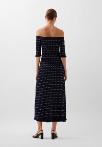 Sini off-the-shoulder dengan garis horizontal putih, tekstur berkerut, lengan tiga perempat, dan hem yang melebar. Dipadukan dengan sepatu hak blok hitam.