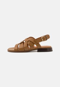 Sandales en cuir marron avec un design entrelacé, talon plat et boucle à la cheville réglable. Texture douce et structure minimaliste.