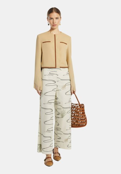 Blusa beige corta con dettagli marroni, abbinata a pantaloni larghi a fantasia in crema con disegni verdi e neri. Borsa a tracolla intrecciata marrone.